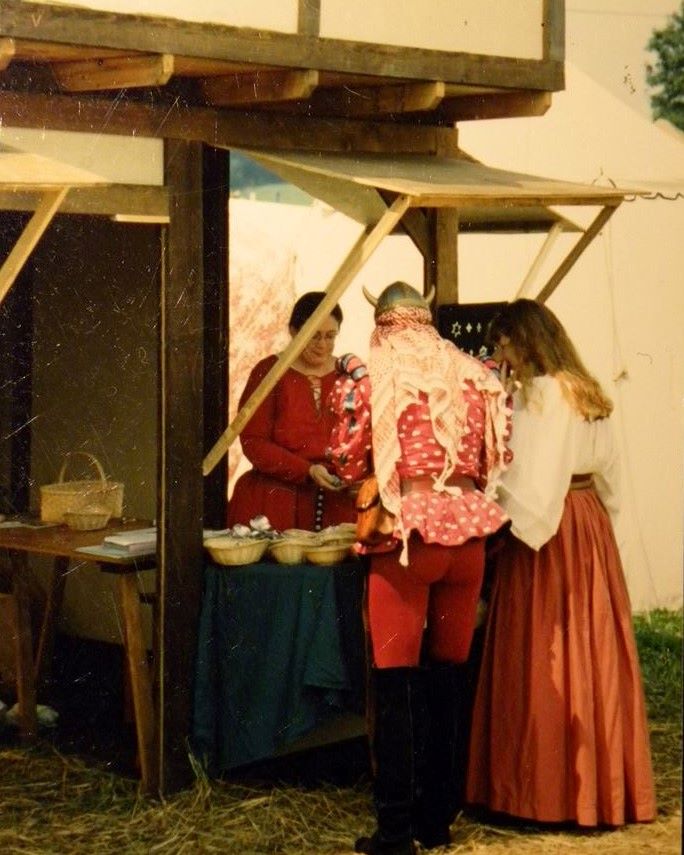 Old photo from pennsic: Marianne waiting on a customer in a horned "Viking" helmet