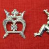 Three brooches with an over M shape. The first is a nude man leaning over to display his anus and penis. The second is a letter M with a crowns and a flower. The third is a grotesque male figure with crowned head, spread legs, and pendant penis.