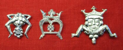 Three brooches with an over M shape. The first is a nude man leaning over to display his anus and penis. The second is a letter M with a crowns and a flower. The third is a grotesque male figure with crowned head, spread legs, and pendant penis.